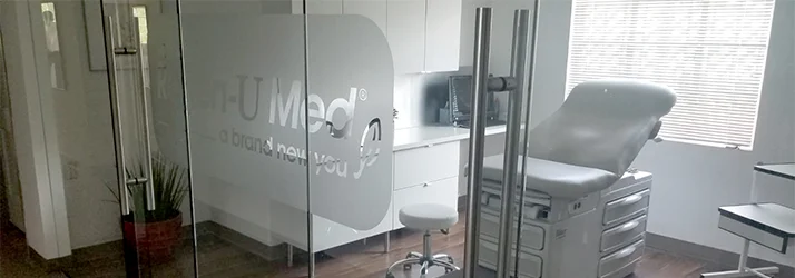 Regenerative Medicine Houston TX About our Clinic A medical exam table is seen through glass doors with Houston Regen-U Med branding